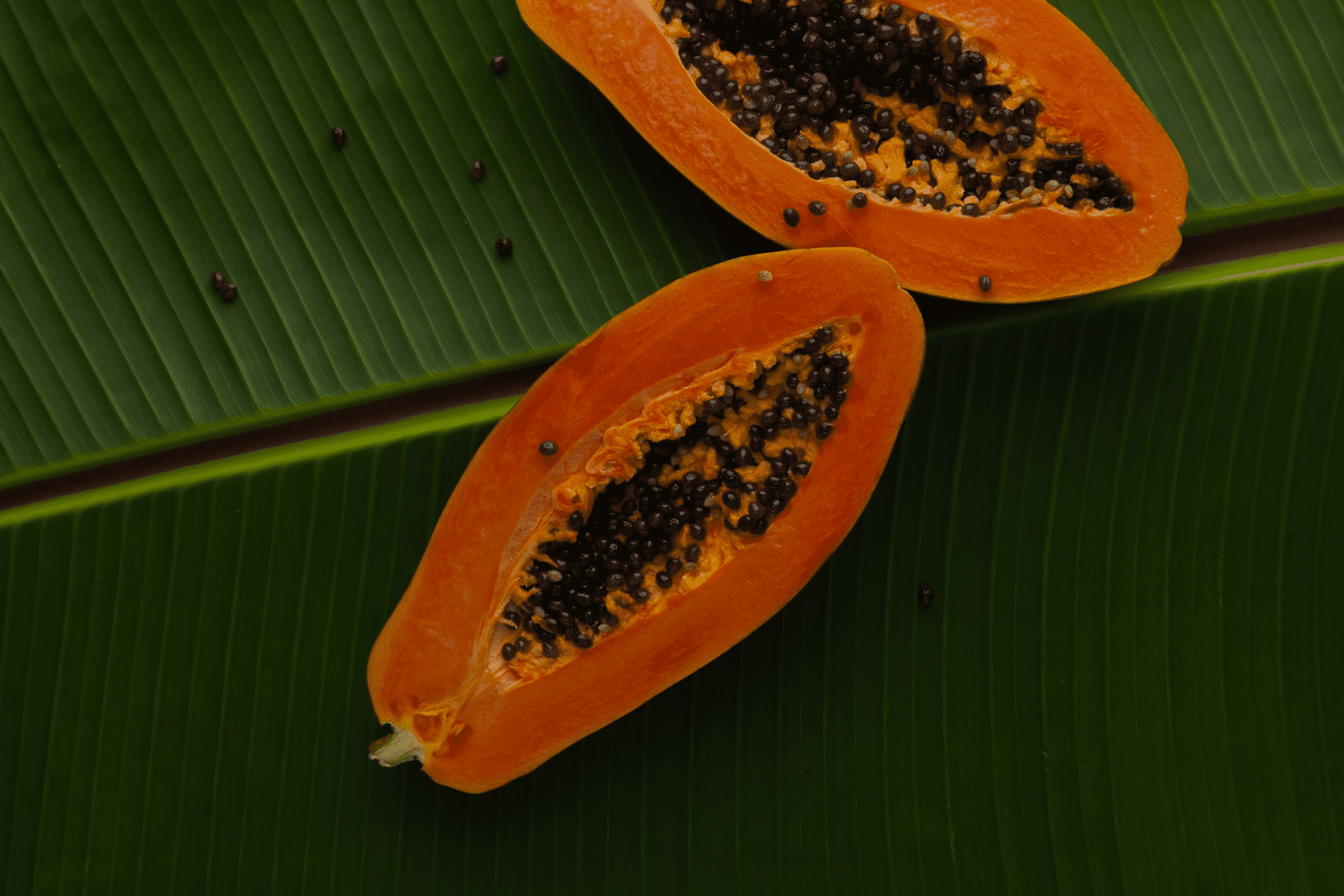 Halved organic papaya on banana leaves, showcasing the natural and healthy tropical fruits offered by Colectivo Orgánico.